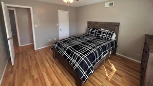 A bedroom with a bed, wooden flooring, a ceiling fan, and a door. - Near Fort Sill Cozy 2-Bedroom Townhouse (Lawton)
