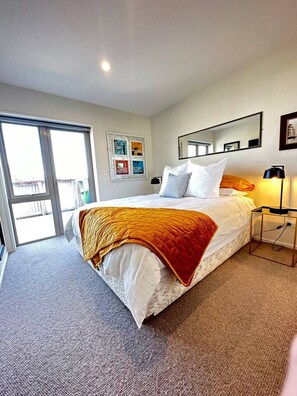 Ein Hotelzimmer mit einem großen Bett, einem Nachttisch, einer Lampe, einem Fenster und einer Tür, die auf einen Balkon führt.