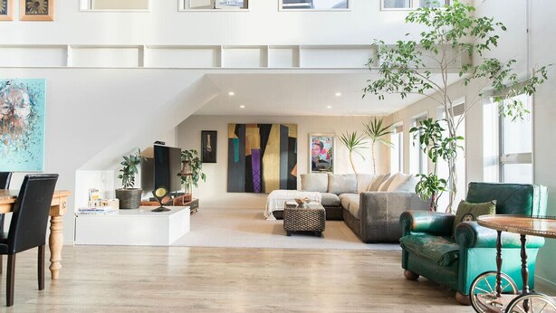 A spacious living area with a high ceiling, a dining area with a wooden table and chairs, and a seating area with a green sofa and a small table. - Stylish Art Loft with Spa & Soaring Ceilings (Christchurch)