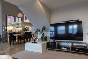Ein modernes Wohnzimmer mit einem großen Flachbildfernseher, einem Essbereich mit Stühlen und einem Tisch sowie einer Treppe, die zu einer oberen Ebene führt.