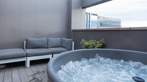 A rooftop terrace with a gray sofa, a hot tub, and a small plant. - Stylish Art Loft with Spa & Soaring Ceilings (Christchurch)
