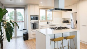 A modern kitchen with white cabinetry, a central island with stools, a microwave, oven, and a gas stove. - Stylish Art Loft with Spa & Soaring Ceilings (Christchurch)