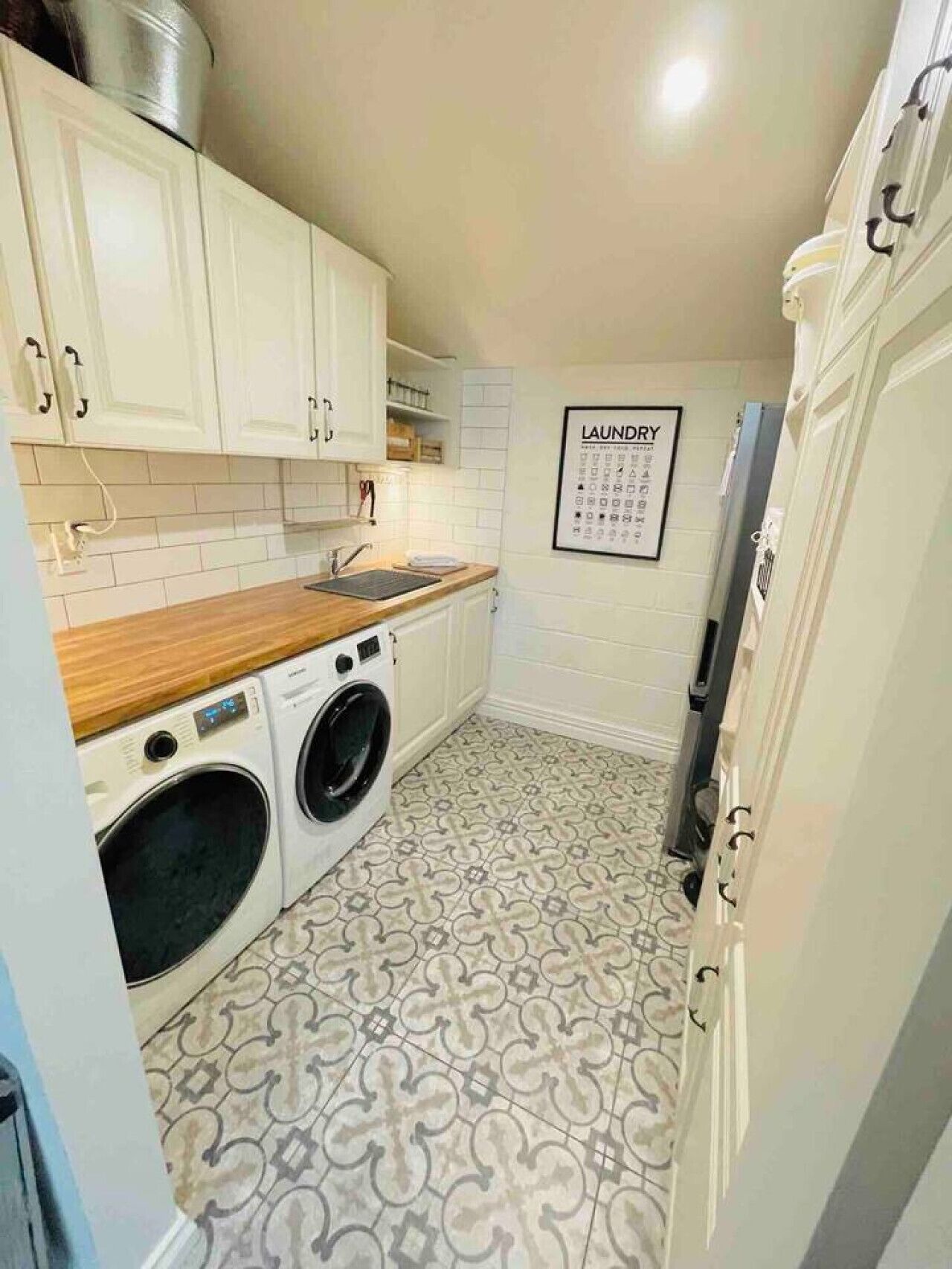 A compact kitchen with white cabinets, a wooden countertop, a washing machine, and a patterned floor.