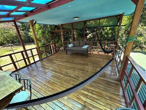 A wooden deck with a covered seating area, a hammock, and a table with chairs. - Montezuma Nicoya Peninsula 3 bedroom house with pool in tropical paradise (Las Delicias, Cobano)