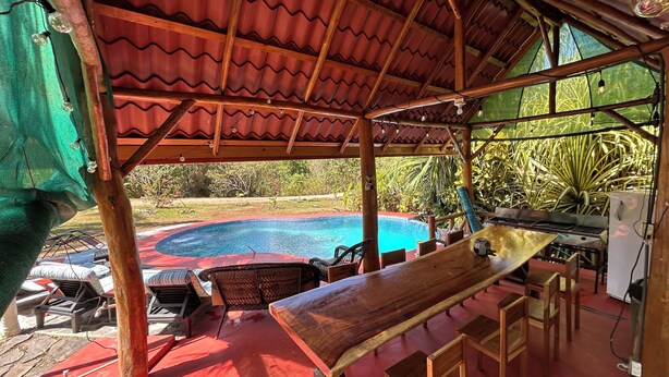 A covered outdoor area with a pool, wooden furniture, and a table. - Montezuma Nicoya Peninsula 3 bedroom house with pool in tropical paradise (Las Delicias, Cobano)
