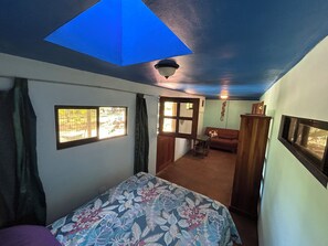 Ein Zimmer mit Bett, Sofa, kleinem Tisch, Fenster und Deckenleuchte.