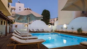 Una piscina con sillas de descanso y sombrillas, rodeada de edificios.