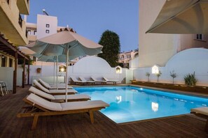 Une piscine entourée de bâtiments, avec des chaises longues et des parasols.