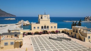 Un edificio costero con una torre de reloj, un patio empedrado y vista al mar.
