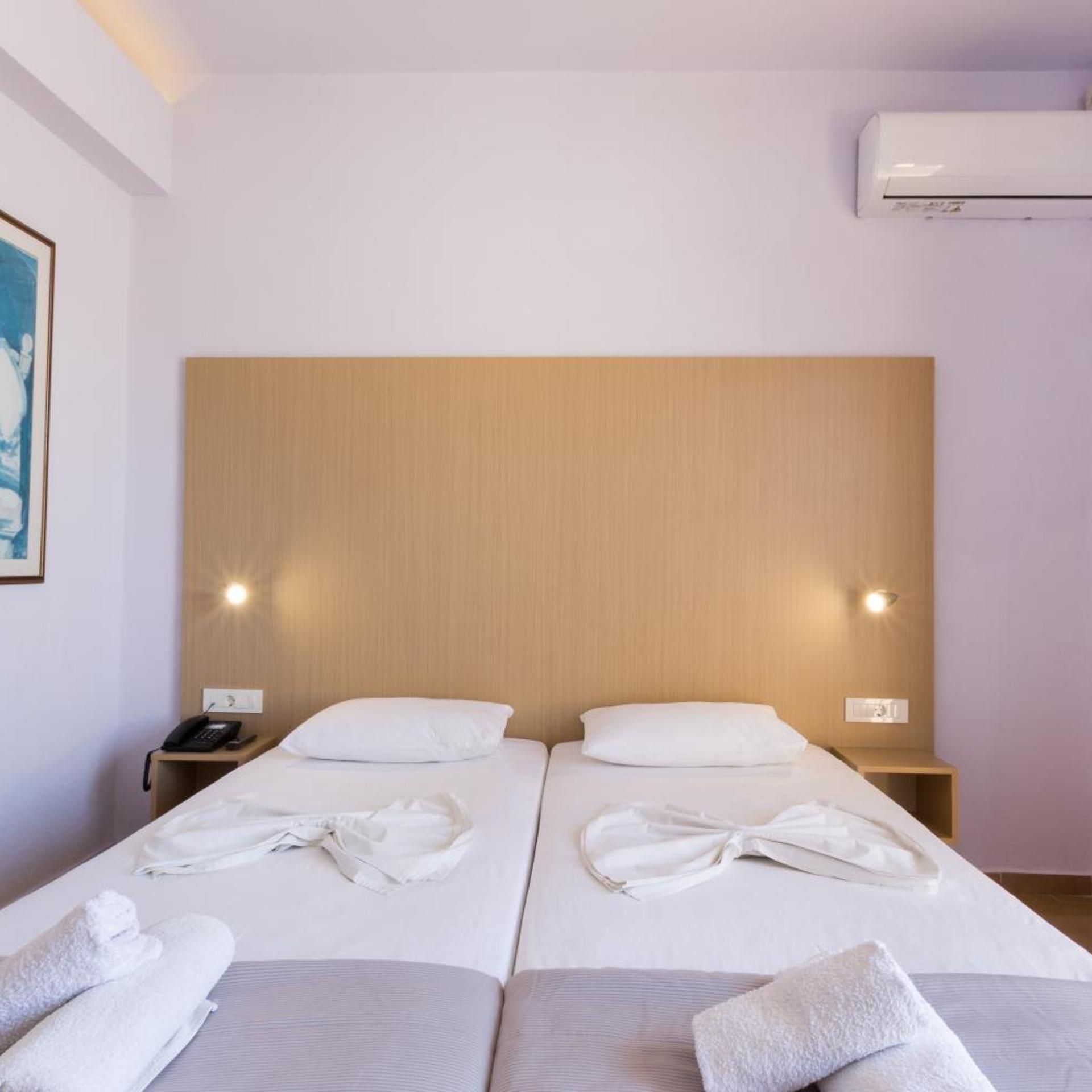 A hotel room with two beds, a bedside telephone, an air conditioning unit, and a painting on the wall.