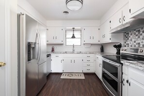 A modern kitchen with white cabinets, stainless steel appliances, and a backsplash with patterned tiles. - Dreamy Dwelling on Matador w/ Gameroom (Amarillo)