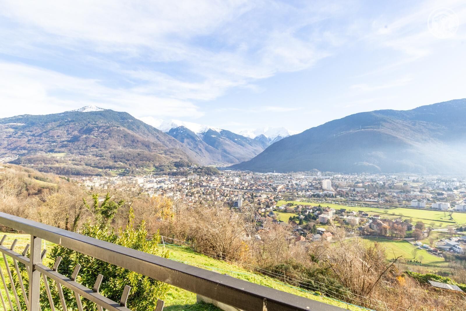 A panoramic view of a town nestled between mountains, with a clear sky and a distant snow-capped peak.