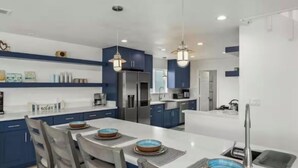 Una cucina moderna con isola centrale, pensili blu, elettrodomestici in acciaio inossidabile e illuminazione a sospensione.