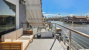 Una terrazza con un letto, angolo relax e ringhiera che si affaccia su un canale con barche ed edifici.