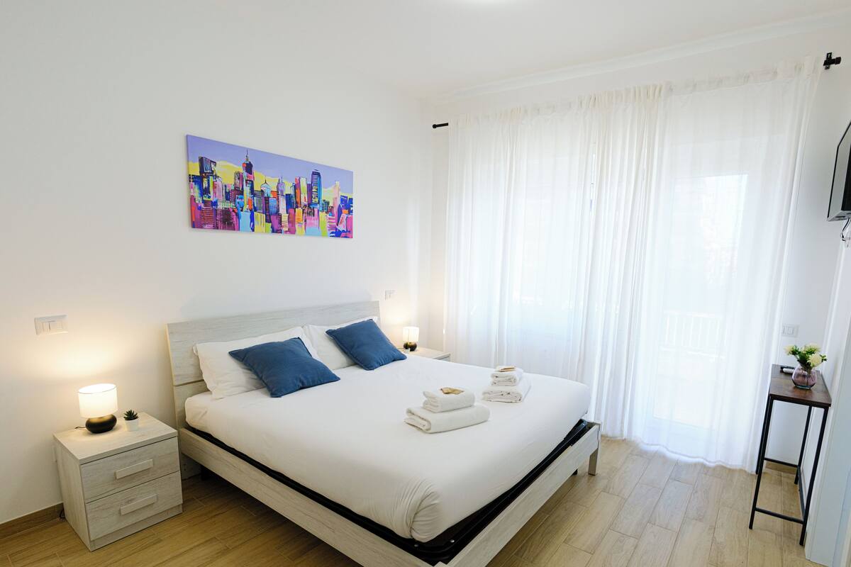 A neatly arranged bedroom with a bed, bedside tables, and a painting on the wall.