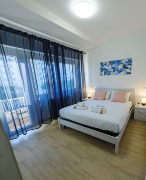 Une chambre à coucher avec un lit, une table de chevet, une lampe, un tableau et une vue sur l’extérieur.