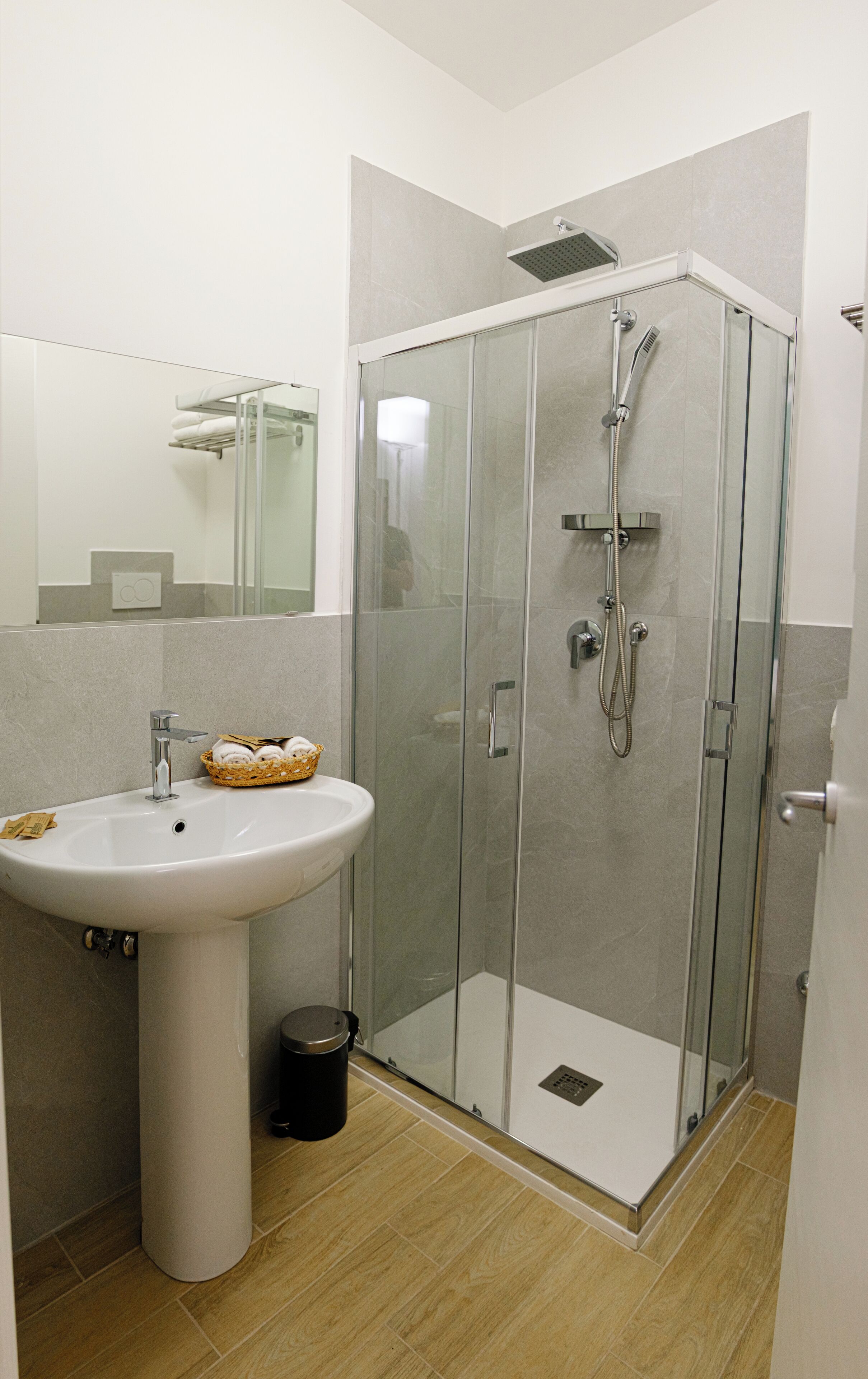 A modern bathroom with a glass-enclosed shower, a pedestal sink, and a mirror above the sink.