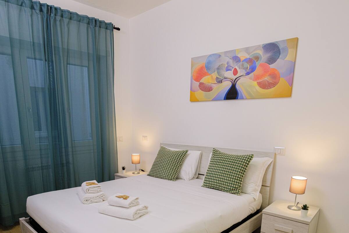 A neatly made bed with pillows, a bedside table with a lamp, and a painting on the wall.