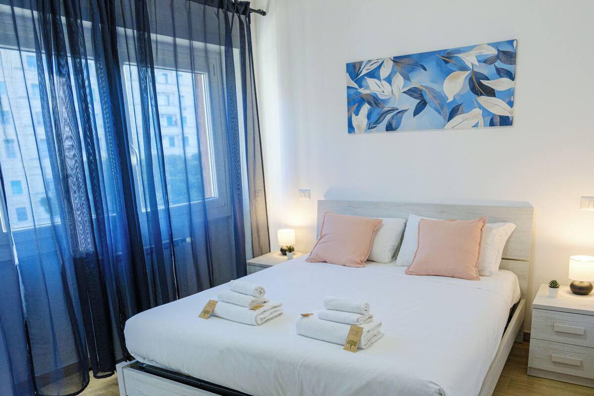 A neatly made bed with towels, a bedside table with a lamp, and a painting on the wall.