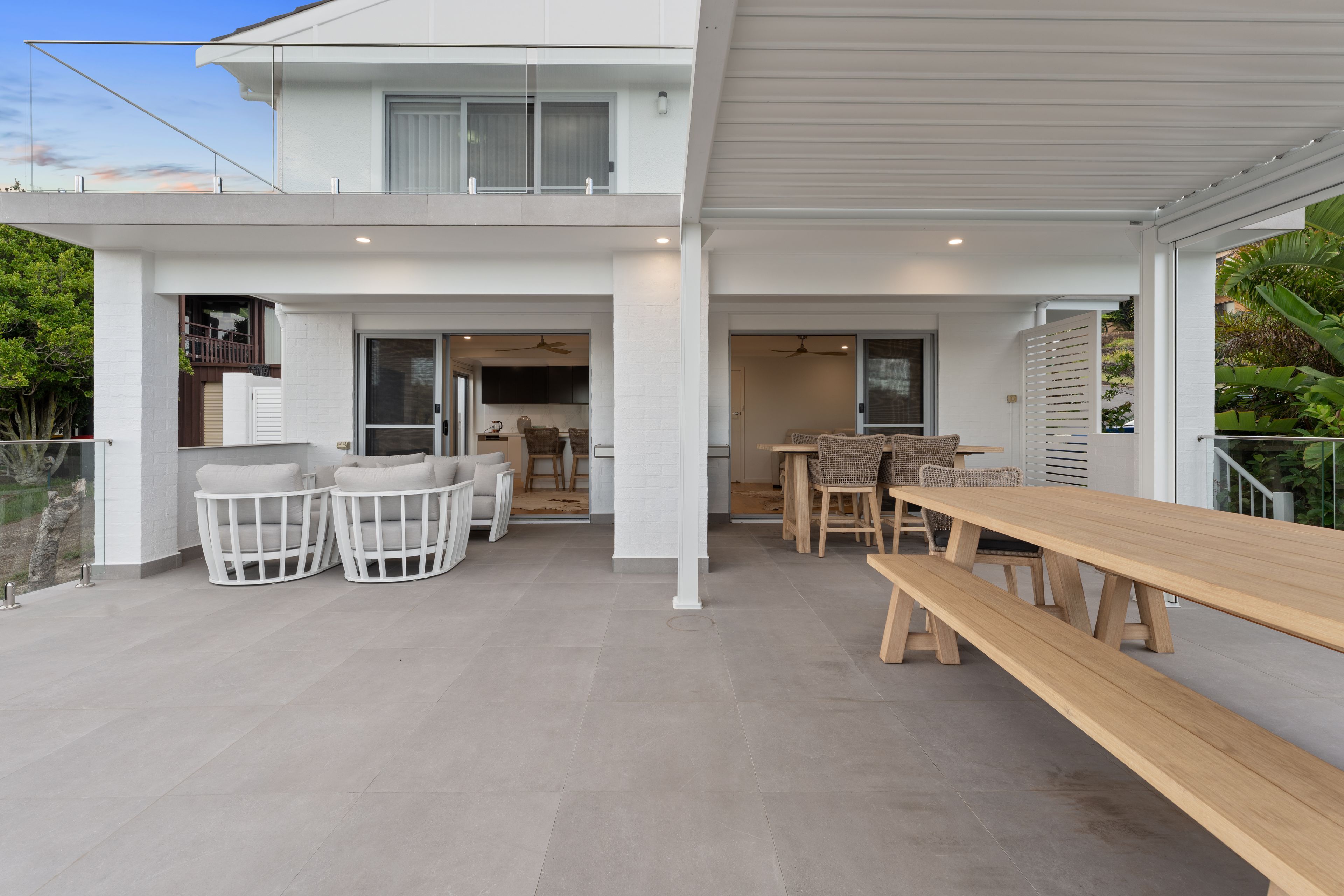 A modern two-story house with a patio area featuring a dining set and a wooden bench.
