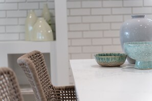 A dining area with wicker chairs, a white table, and ceramic bowls and vases. - Sea Sage Coastal Retreat in Fingal Bay (Fingal Bay)