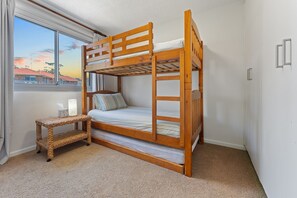 A bunk bed with a small bedside table, a window with a view of houses, and a carpeted floor. - Shoal Bay Sunrise Waterfront Apartment Nelson Bay (Nelson Bay)