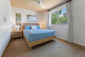 A bedroom with a bed, a nightstand, a mirror, a window with curtains, and a ceiling fan. - Shoal Bay Sunrise Waterfront Apartment Nelson Bay (Nelson Bay)