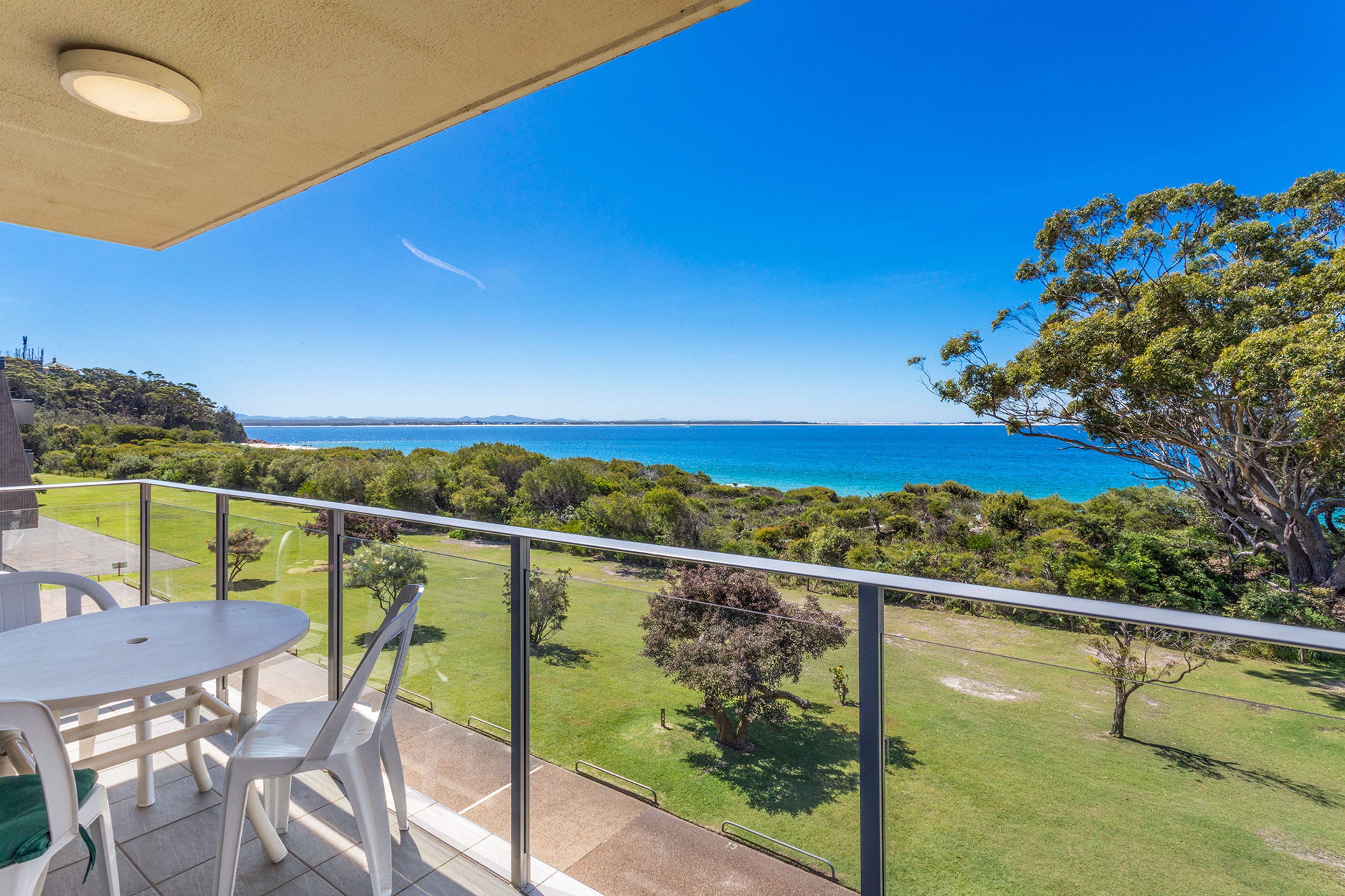 A balcony with a view of the ocean, a table, chairs, and a railing.