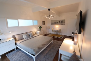 A modern bedroom with a bed, bedside tables, a desk, a chair, a TV, and a ceiling fan. - Front-Row Hollywood Sign Views -Modern Glass Villa (Los Angeles)