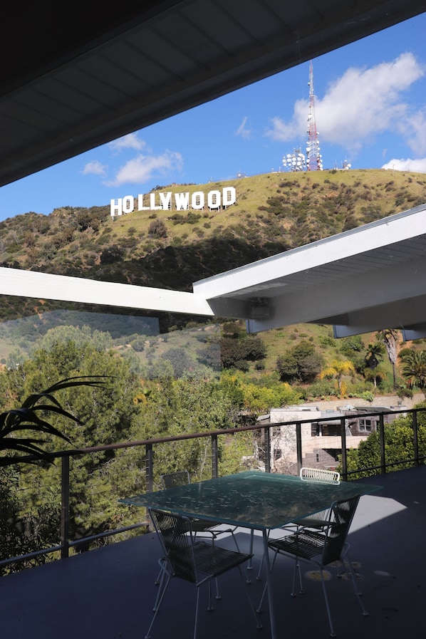 A balcony with a table and chairs, overlooking a hill with the Hollywood sign and a radio tower. - Front-Row Hollywood Sign Views -Modern Glass Villa (Los Angeles)