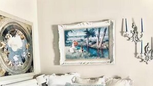 A bedroom with a bed, pillows, a painting, and wall decor.
