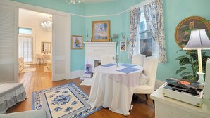 A room with a fireplace, a chandelier, a round table with a white tablecloth, and a patterned rug.
