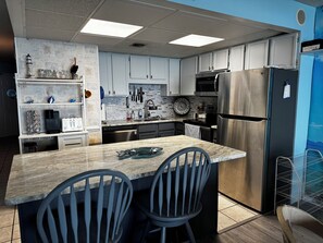 A modern kitchen with white cabinets, a stainless steel refrigerator, and a marble island with two chairs.