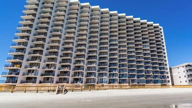 A high-rise hotel with multiple balconies, a flat facade, and a clear blue sky in the background. - Beachfront condo w/ balcony in wonderful Garden City Beach (Murrells Inlet)