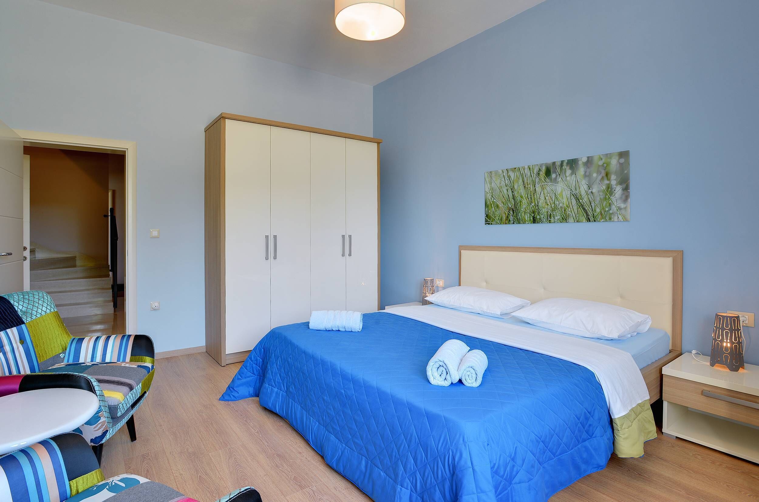 A bedroom with a bed, a chair, a wardrobe, and a painting on the wall.
