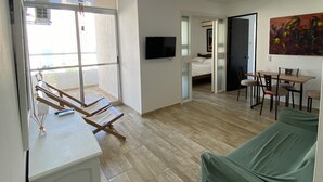 A spacious living area with a green sofa, wooden flooring, a TV mounted on the wall, and a balcony with a chair. - Ocean view apartment (Cartagena de Indias)