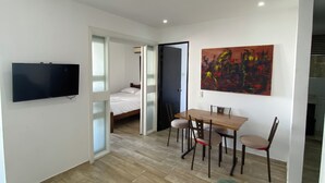 A modern living room with a flat-screen TV, a dining table with chairs, a bed, and a colorful abstract painting on the wall. - Ocean view apartment (Cartagena de Indias)