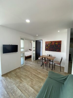 A modern living room with a flat-screen TV, a dining table with chairs, a bed, and a colorful abstract painting on the wall. - Ocean view apartment (Cartagena de Indias)