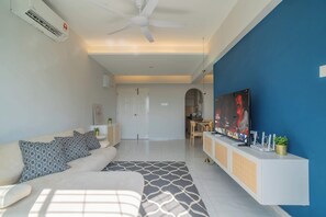 Ein modernes Wohnzimmer mit Sofa, Fernseher, Deckenventilator und einer Küche im Hintergrund.