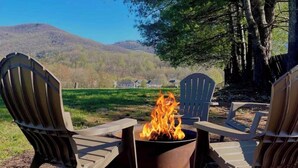 Deux fauteuils Adirondack sont placés face à un foyer extérieur, avec une vue sur les montagnes en arrière-plan.