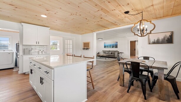 Une cuisine moderne avec des meubles blancs, un plafond en bois et un coin repas comprenant une table et des chaises en bois.