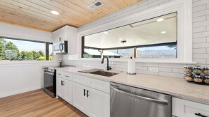 Une cuisine moderne avec des meubles blancs, des appareils en acier inoxydable, une grande fenêtre donnant sur les montagnes et un plafond en bois.