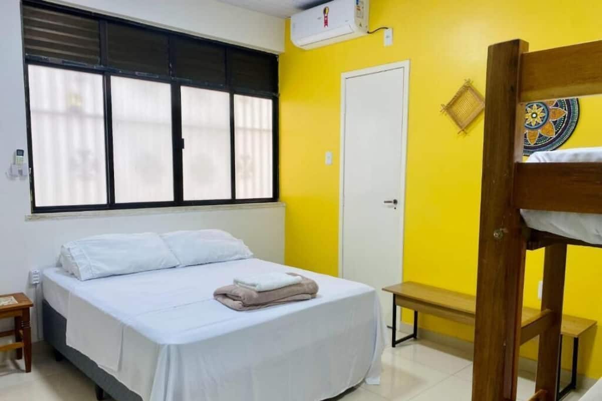 Um quarto com uma cama, um banco, uma porta e uma janela com persianas.
