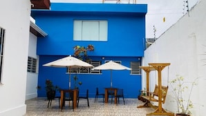 Une cour avec un bâtiment bleu, du mobilier d’extérieur et des plantes en pot.