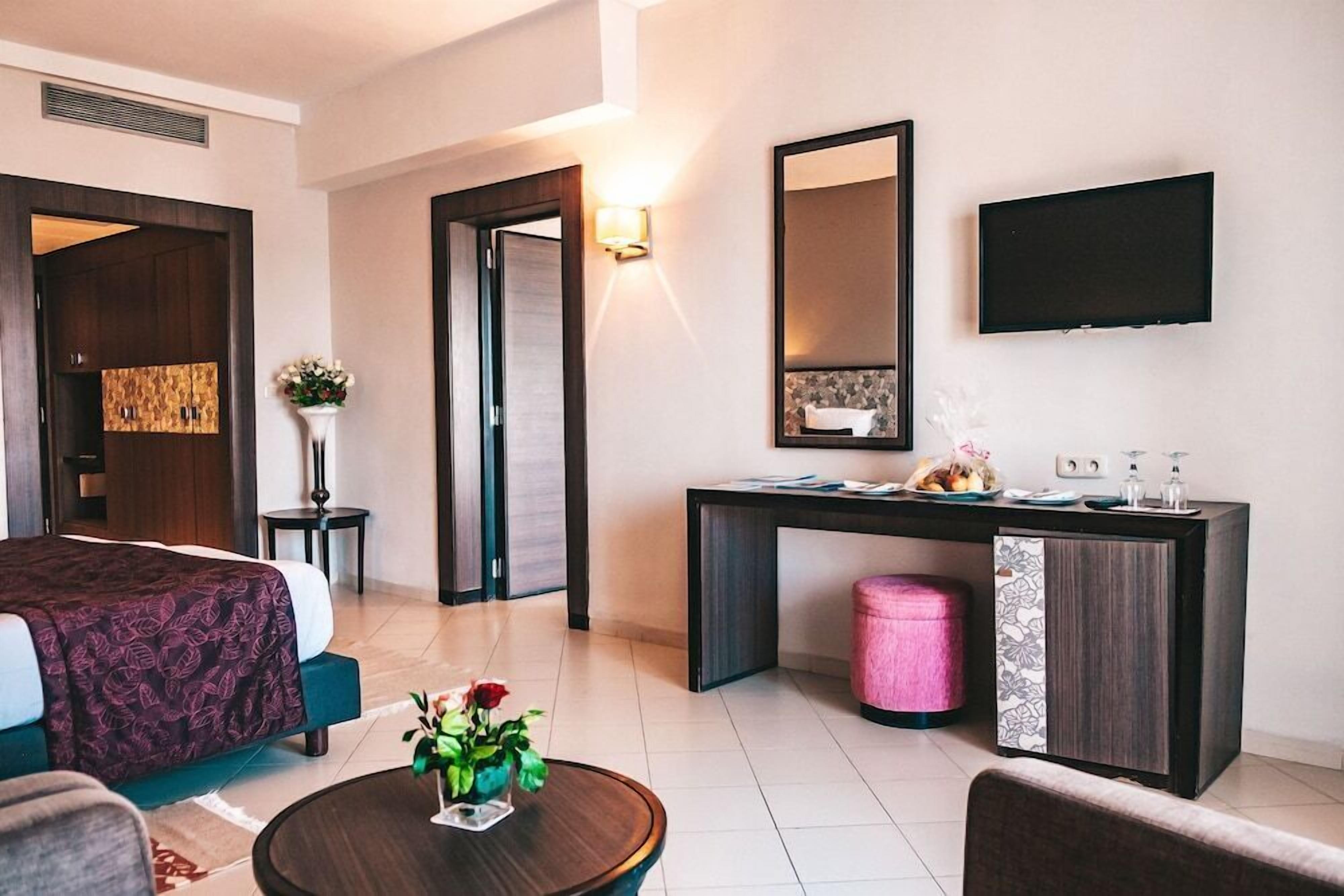 A hotel room with a bed, a desk, a television, and a small table with flowers.
