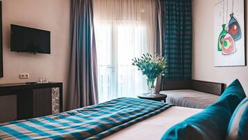 A hotel room with a bed, bedside table, TV, and a window with curtains.