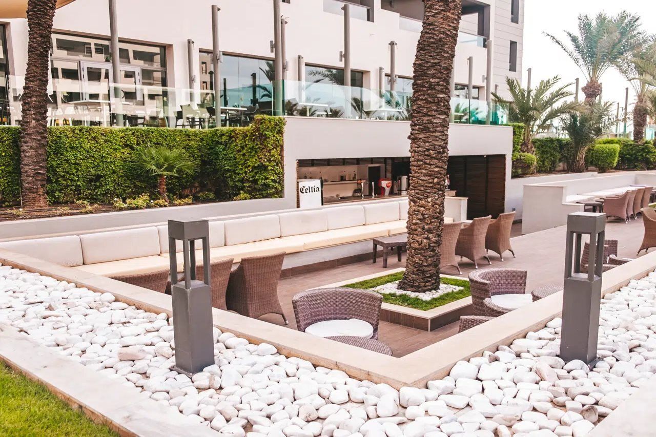 An outdoor seating area with a long bench, wicker chairs, and a small garden with white pebbles.