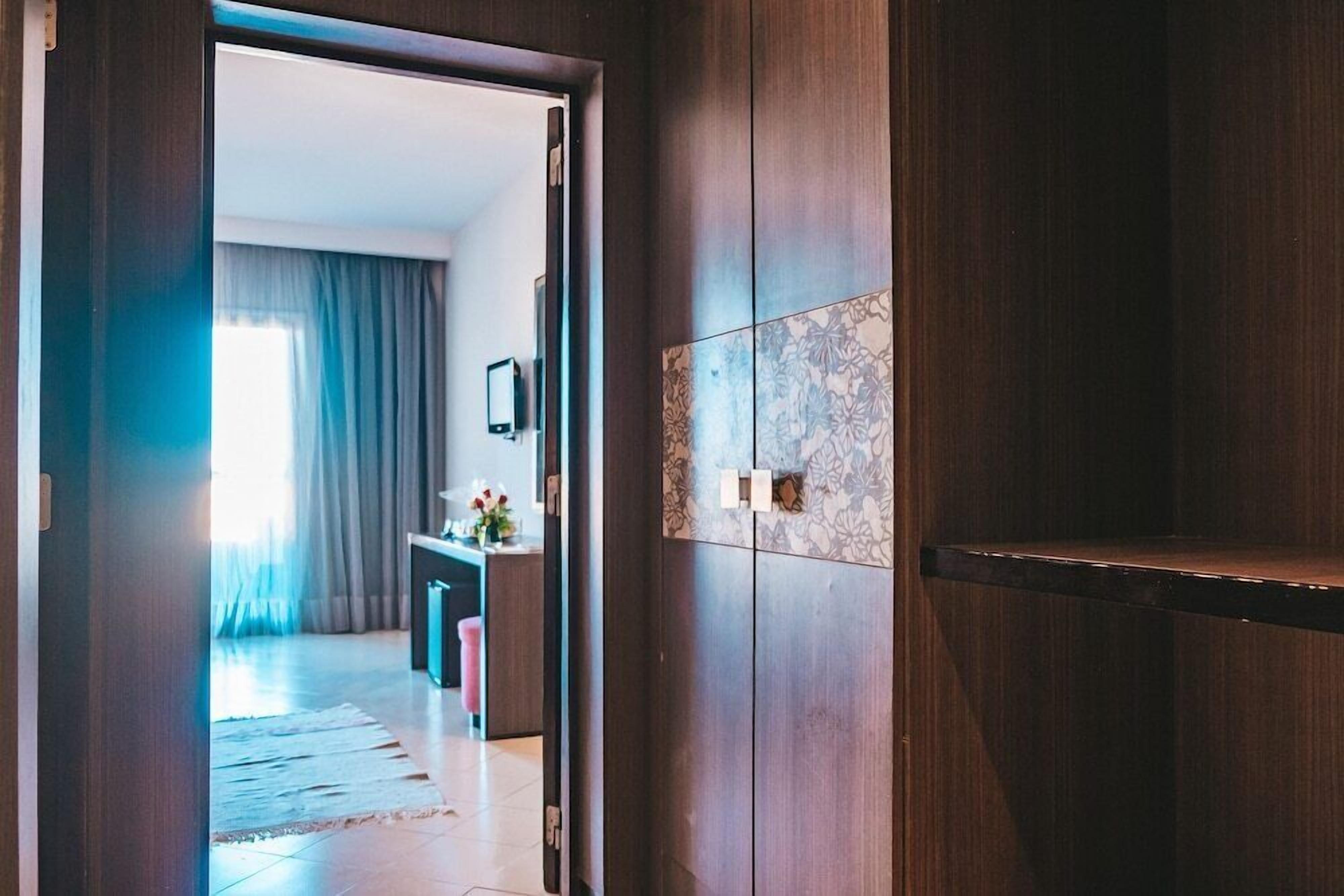 Puerta de madera que da a una habitación con salpicadero de azulejos y parte visible de una sala de estar con sofá y mesa de centro.