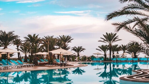 A pool area with lounge chairs and umbrellas, surrounded by palm trees.