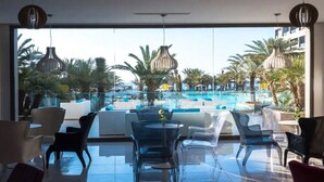 A modern indoor pool area with clear glass walls, lounge chairs, and hanging pendant lights.